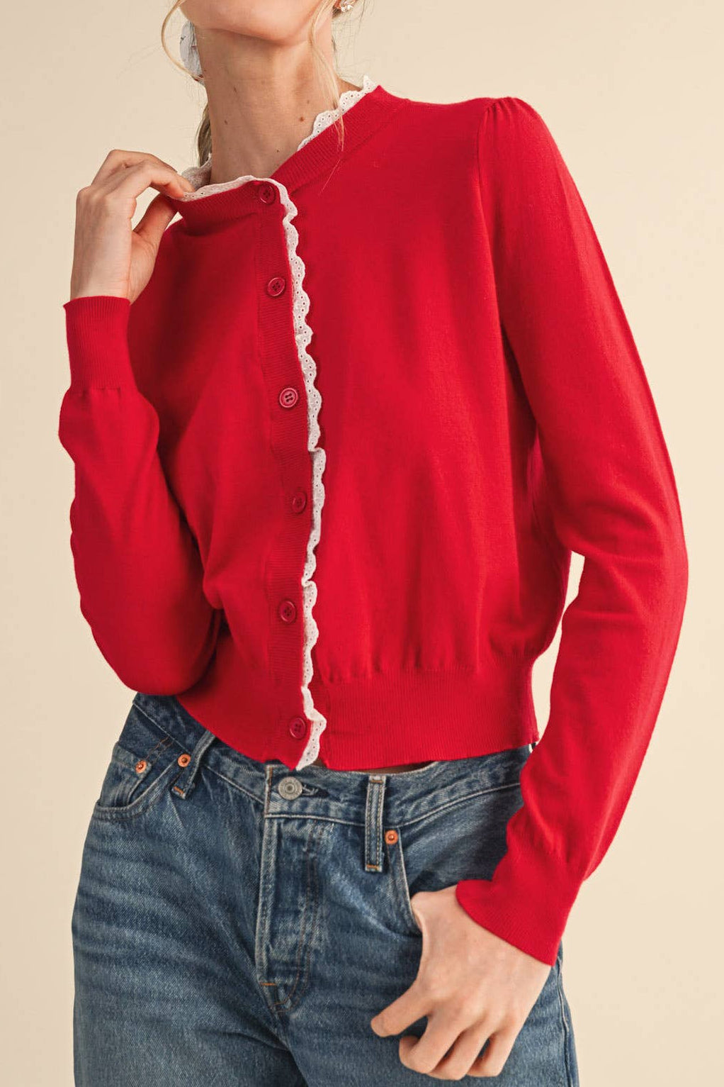 Red cardigan with white trim worn by a person on a beige background