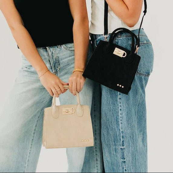 Two women holding handbags against a plain background
