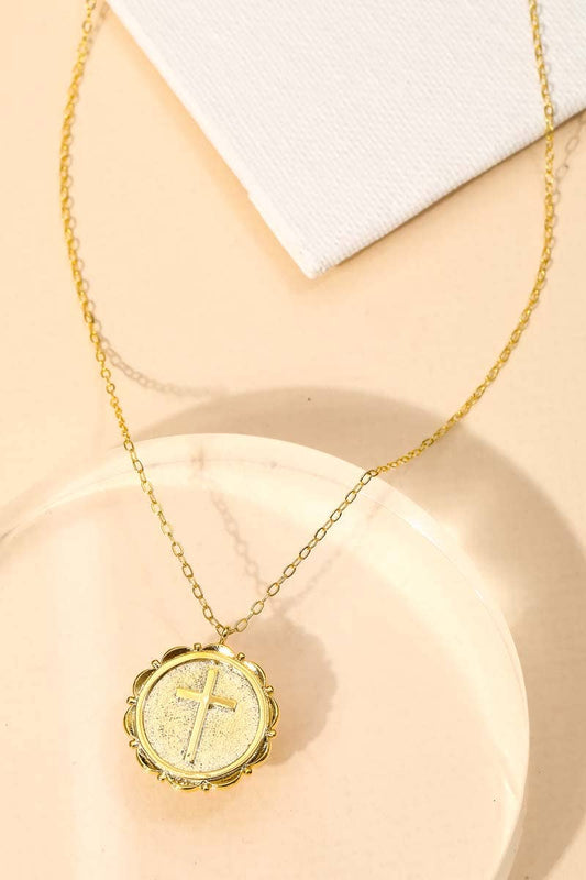 Gold necklace with a round pendant featuring a cross on a beige surface