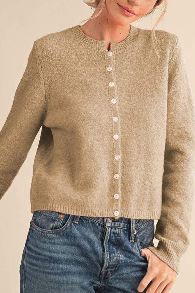 Person wearing a beige cardigan and blue jeans on a plain background