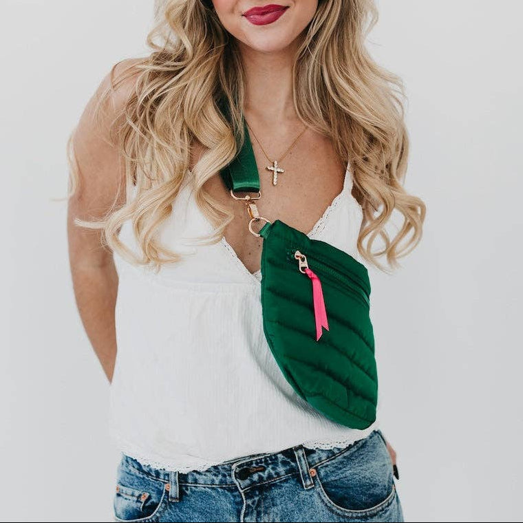 Woman wearing a green crossbody bag with a pink accent on a plain background