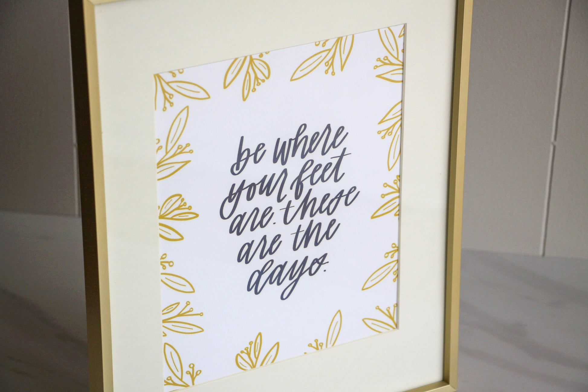 Framed print with motivational hand lettered quote 'be where your feet are these are the days' on a light background, for moms or anyone wanting to stay present