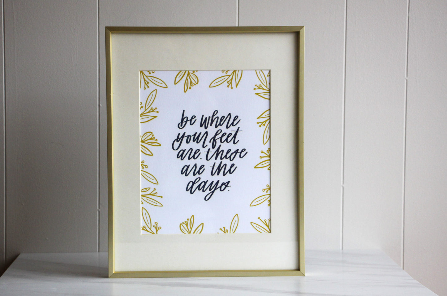 Framed print with motivational hand lettered quote 'be where your feet are these are the days' on a light background, for moms or anyone wanting to stay present