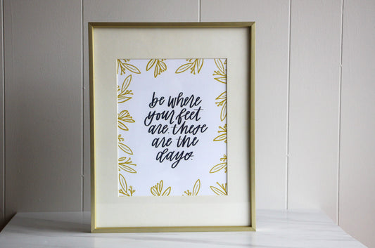 Framed print with motivational hand lettered quote 'be where your feet are these are the days' on a light background, for moms or anyone wanting to stay present