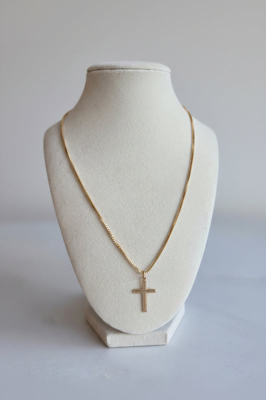 Gold necklace with a cross pendant on a mannequin bust against a plain background