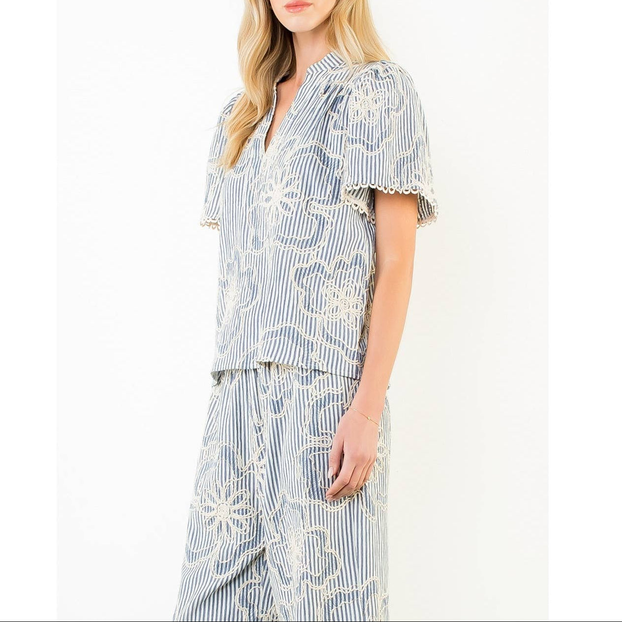 Woman wearing a blue and white striped top and pant set with floral patterns on a white background