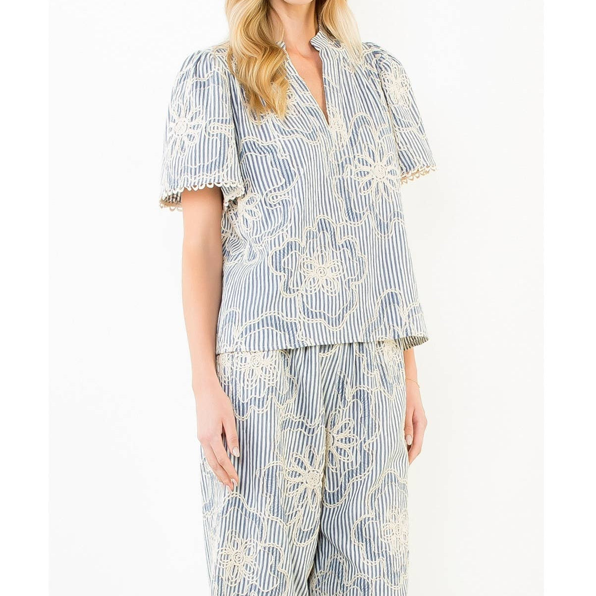 Woman wearing a blue and white striped blouse and pant set with floral embroidery on a white background