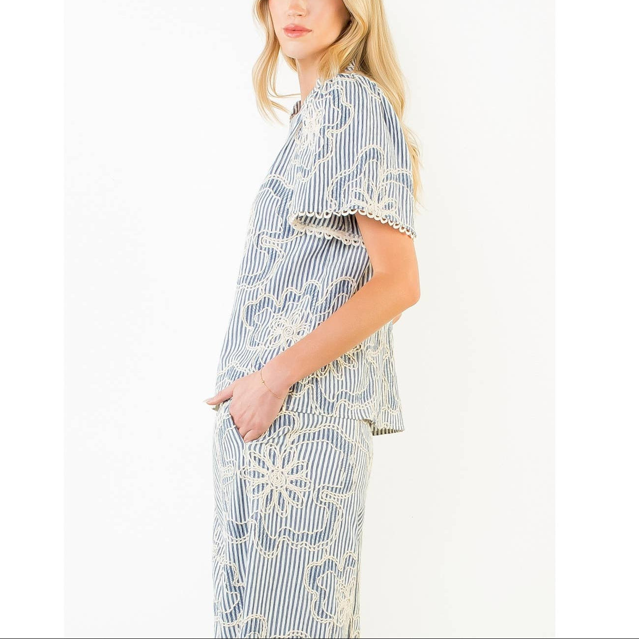 Side view of a woman wearing a blue and white striped outfit with lace details on a white background