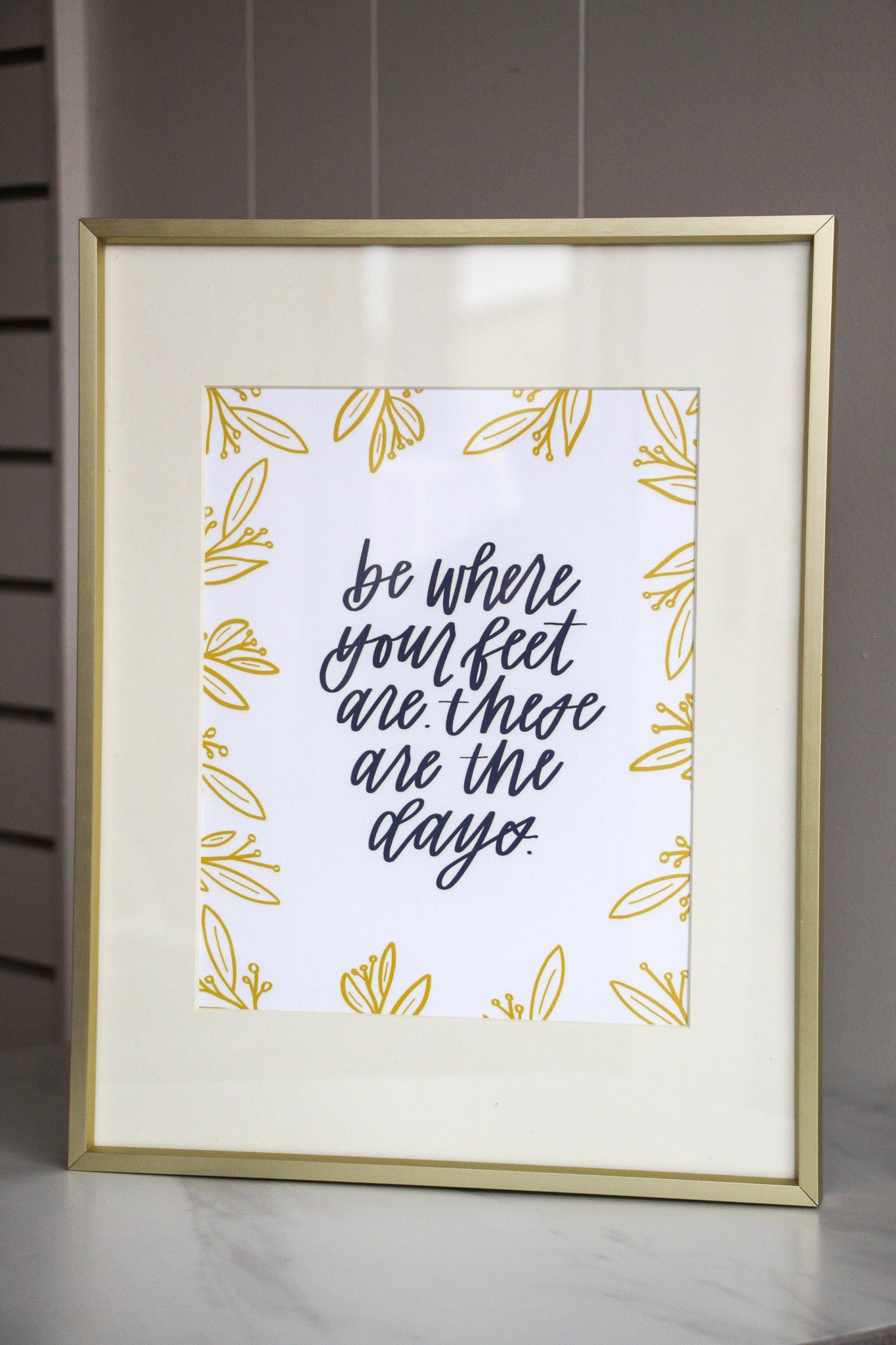 Framed print with motivational hand lettered quote 'be where your feet are these are the days' on a light background, for moms or anyone wanting to stay present