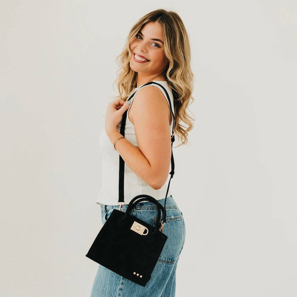 Woman holding a black handbag against a plain background
