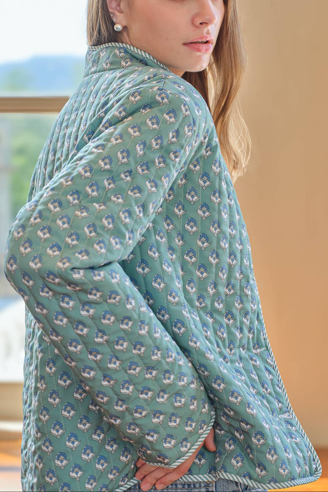 Woman wearing a blue green quilted jacket with a subtle pattern indoors.