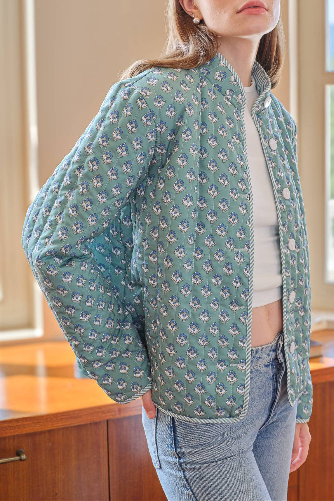 Woman wearing a green quilted jacket with a floral pattern in an indoor setting.
