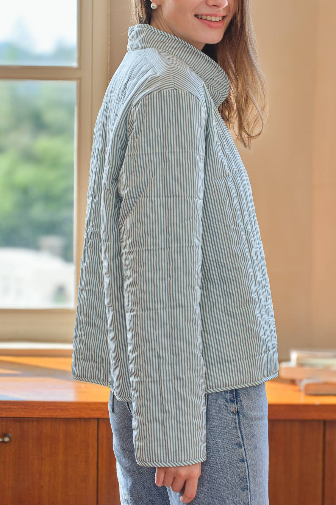 Woman wearing a green striped puffer jacket indoors with a window in the background